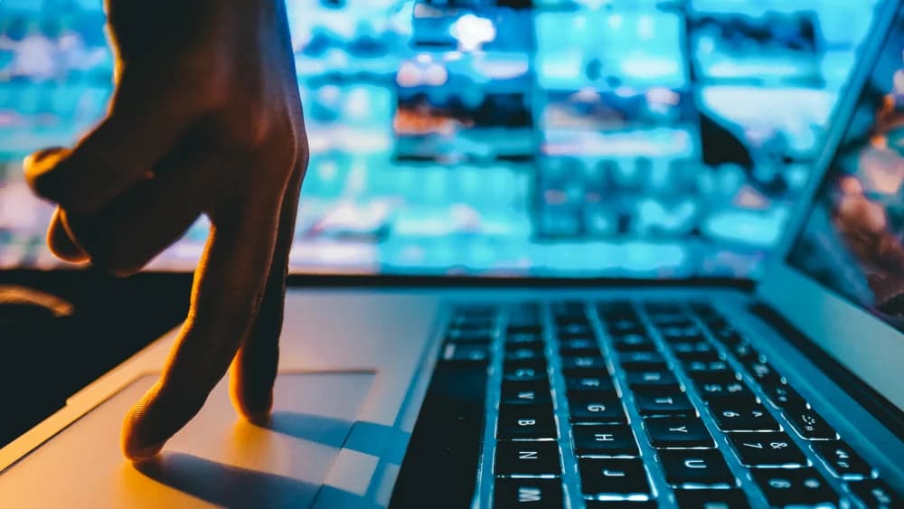 Mano sobre el teclado de un portátil con luz azul